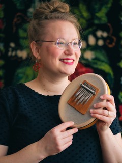 Hymyilevä nainen, jolla on käsissään pyöreä, näppäiltävä instrumentti.