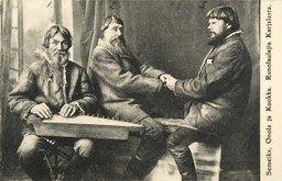 Harmaasävyinen postikortti. Kuvassa yksi mies soittaa kannelta ja katsoo kohtisuoraan kameraan, kaksi miestä istuu vastakkain pitäen toisiaan käsistä ristikkäin.