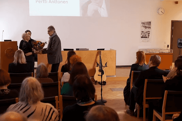 Yleisö taputtaa, kun kukkakimppu ja palkinto ojennetaan Pertti Anttoselle.